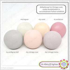 Może przedstawiać: Pięć okrągłych gałek w różnych pastelowych kolorach, w tym jasnoszary, jasnoróżowy, jasnozielony, jasnofioletowy i jasnożółty. Gałki są oznaczone numerami i nazwami kolorów, takimi jak #4 antikgrau hell, #55 vintage rosé, #10 ingwer, #42 vintage malve i #33 sand. Tekst "Möbelknopf im Vintage Look matte Kreidefarben in verschiedenen Farben erhältlich" znajduje się w górnej części obrazu.