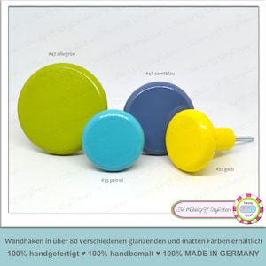 Könnte beinhalten: Vier Holzknöpfe in verschiedenen Farben: Olivgrün, Blau, Türkis und Gelb. Die Knöpfe sind rund und haben eine glatte Oberfläche. Der gelbe Knopf hat eine Schraube auf der Rückseite.