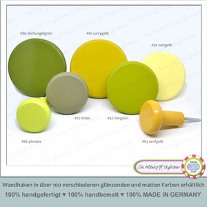Peut inclure: Assortiment de boutons ronds en bois dans différentes nuances de vert et de jaune. Les boutons sont peints dans des couleurs telles que pistache, kaki, vert olive, jaune curry et jaune moutarde. Les boutons sont étiquetés avec des numéros et des noms de couleurs. Le texte "Die Möbelgriff Stylisten" est visible dans le coin inférieur droit de l'image.