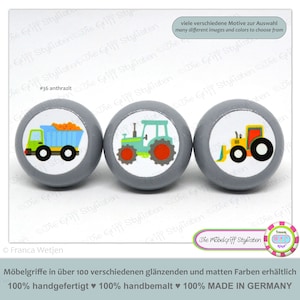 May include: Three gray wooden knobs with colorful illustrations of a dump truck, a tractor, and a bulldozer. The knobs are labeled "#36 anthrazit" and "Die Möbelgriff Stylisten".