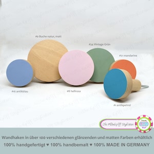 Könnte beinhalten: Sortiment an Wandhaken aus Holz in verschiedenen Farben, darunter hellblau, rosa, grün, orange und naturbelassenes Holz. Die Haken sind rund und haben einen Durchmesser von etwa 7,5 cm. Der Text "Die Möbelgriff Stylisten" ist im Bild sichtbar.