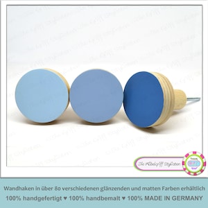Peut inclure: Trois crochets muraux en bois avec des cercles peints en bleu. Les crochets sont fixés à une base en bois. Le texte "Die Möbelgriff Stylisten" est visible sur l'image.