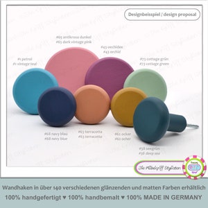 Könnte beinhalten: Eine Auswahl an farbenfrohen Holzknöpfen in verschiedenen Größen und Farbtönen, darunter Petrol, Marineblau, Terrakotta und Ocker. Das Bild enthält deutschen Text, der besagt, dass die Knöpfe in über 140 Farben erhältlich sind und in Deutschland handgefertigt werden.