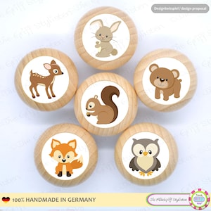 May include: A set of six wooden cabinet knobs with woodland animal designs. Each knob features a different animal: a deer, a rabbit, a squirrel, a bear, a fox, and an owl. The knobs are labeled "100% HANDMADE IN GERMANY".