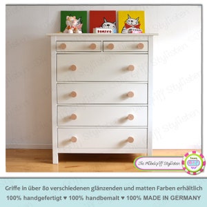 Könnte beinhalten: Weiße Kommode mit sechs Schubladen und Holzgriffen. Die Kommode hat eine helle Holzoptik und ist in Deutschland hergestellt. Die Kommode ist mit drei kleinen Katzenbildern verziert.
