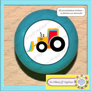 Puede incluir: Un pomo redondo turquesa con un círculo blanco en el centro. El círculo blanco presenta un tractor de juguete amarillo y rojo con ruedas negras. El texto "45 verschiedene Farben + 19 Motive zur Auswahl" está impreso encima del tractor. El texto "Die Möbelgriff Stylisten" está impreso debajo del tractor.
