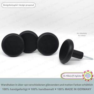 Może przedstawiać: Cztery czarne drewniane gałki z wkrętem z tyłu. Gałki są okrągłe i mają gładkie wykończenie. Tekst "#27 ebenholz #27 ebony" jest widoczny na zdjęciu. Tekst "Die Möbelgriff Stylisten" jest również widoczny na zdjęciu.