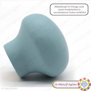 May include: A light blue knob with a textured surface. The knob is made of wood and has a vintage look. The text "Möbelknopf im Vintage Look matte Kreidefarben in verschiedenen Farben erhältlich" is visible in the image.