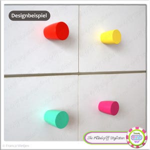 Könnte beinhalten: Vier farbige, zylindrische Holzknauf-Türgriffe in Rot, Gelb, Türkis und Pink. Die Griffe haben eine glatte Oberfläche und sind an einer weißen Oberfläche montiert.