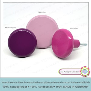 Peut inclure: Trois boutons en bois de différentes couleurs : aubergine, mauve et fuchsia. Les boutons sont ronds et ont une finition lisse. Le texte "Die Möbelgriff Stylisten" est visible sur l’image.