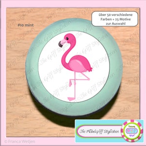 Könnte beinhalten: Ein runder, türkisfarbener Knopf mit einer weißen Mitte, auf der ein rosa Flamingo abgebildet ist. Der Text "#10 mint" ist oben links sichtbar. Der Text "über 50 verschiedene Farben + 25 Motive zur Auswahl" ist oben rechts sichtbar.