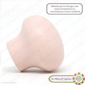 May include: A light pink ceramic knob with a rounded, slightly asymmetrical shape. The knob is designed for use on furniture and has a matte finish. The text "Möbelknopf im Vintage Look matte Kreidefarben in verschiedenen Farben erhältlich" is visible in the image.