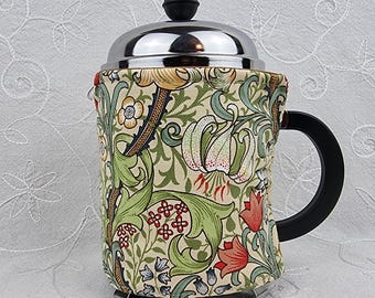 Könnte beinhalten: Eine French-Press-Kaffeemaschine mit einer floral gemusterten Hülle. Die Hülle hat einen cremefarbenen Hintergrund mit grünen Blättern, roten und weißen Blumen. Die Kaffeemaschine hat einen schwarzen Griff und einen silbernen Deckel.