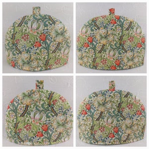 K&ouml;nnte beinhalten: Vier Teekannen-&Uuml;berz&uuml;ge mit einem floralen Muster. Das Muster zeigt Lilien, Bl&auml;tter und kleine rote Bl&uuml;ten auf cremefarbenem Hintergrund.