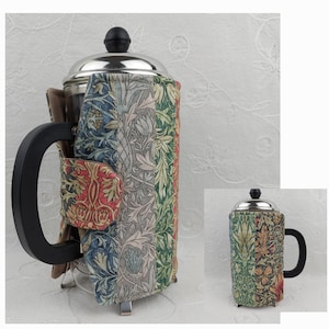 May include: A stainless steel French press coffee maker with a black handle and a colorful fabric cozy. The cozy features a floral pattern in shades of red, blue, green, and gray. The coffee maker has a black knob on top.