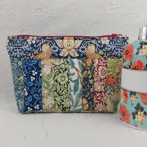 May include: A patchwork cosmetic bag with a red zip and a floral design. The bag features various fabric patterns, including birds and botanical motifs. A matching floral-patterned soap dispenser is next to the bag.