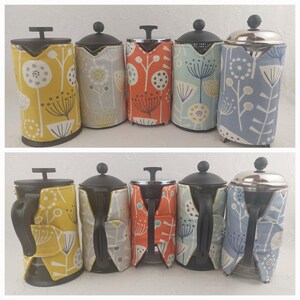 May include: Six French press coffee makers with fabric covers. The covers are in various patterns of yellow, orange, blue, and grey with a floral design.