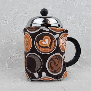 May include: A French press coffee maker with a brown and white patterned cozy featuring coffee cup designs. The cozy has a black handle and a silver lid with a black knob. The coffee maker is designed to hold approximately 34 ounces.