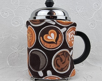 Könnte beinhalten: Eine French-Press-Kaffeemaschine mit einer braun-weiß gemusterten Hülle mit Kaffeetassen-Designs. Die Kaffeemaschine hat einen schwarzen Griff und einen silbernen Deckel mit einem schwarzen Knopf. Sie fasst etwa 1 Liter.