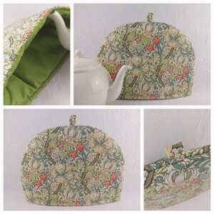 K&ouml;nnte beinhalten: Ein gr&uuml;ner und cremefarbener Teekoscher mit einem Blumenmuster. Der Koscher ist kuppelf&ouml;rmig und hat einen Griff oben. Das Muster zeigt stilisierte Blumen, Bl&auml;tter und Stiele in Gr&uuml;n-, Creme-, Rot- und Blaut&ouml;nen.