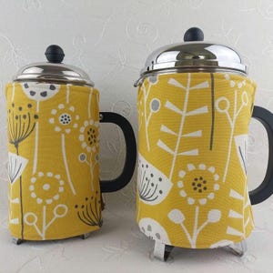 May include: Two yellow and gray patterned fabric coffee press covers. The covers are made of a soft, cotton fabric with a floral design. The coffee presses are not included.