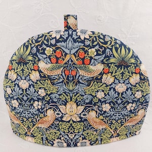 May include: A blue and green tea cozy with a floral pattern and birds. The pattern includes strawberries and leaves.