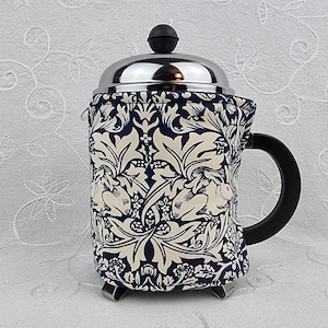 May include: A stainless steel French press coffee maker with a black handle and lid. The coffee maker is covered with a fabric cozy featuring a navy blue and cream floral pattern. The cozy adds a decorative touch and helps to insulate the coffee.