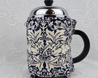 Könnte beinhalten: Eine French Press Kaffeemaschine aus Edelstahl mit schwarzem Griff und Deckel. Die Kaffeemaschine ist mit einem Stoffbezug mit einem marineblauen und cremefarbenen Blumenmuster versehen. Der Bezug verleiht eine dekorative Note und isoliert den Kaffee.