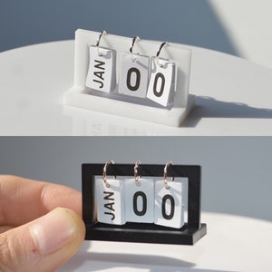 May include: A white and a black desktop calendar with flippable numbers and a month display. The calendar displays the month "JAN" and the numbers "00".