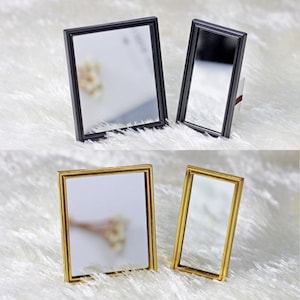 Peut inclure: Quatre miroirs miniatures avec des cadres différents. Deux miroirs ont des cadres noirs et deux miroirs ont des cadres dorés. Les miroirs sont tous rectangulaires et ont une surface réfléchissante.