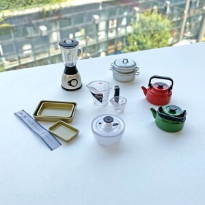 May include: A set of miniature kitchen appliances and cookware, including a blender, a pot, a kettle, measuring cups, baking pans, and a food processor. The items are all in different colors, including silver, red, green, and clear.