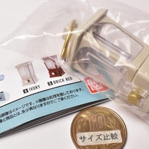 May include: A white and clear plastic miniature model of a vintage music box with a gold-colored top. The model is packaged in a clear plastic bag with a printed instruction sheet. The instruction sheet shows the model in different colors, including ivory and brick red. The sheet also includes a size comparison image with a Japanese 100 yen coin.
