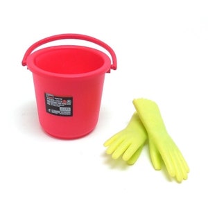 May include: A red plastic bucket with a handle and a pair of yellow rubber gloves. The bucket has a label on the side. The gloves are lying next to the bucket.