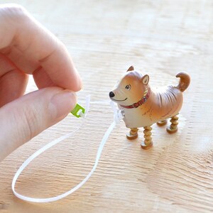 Pode incluir: Um c&atilde;o de brinquedo castanho e branco com pernas de madeira e uma trela branca. O c&atilde;o est&aacute; usando uma coleira vermelha.