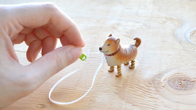 Pode incluir: Um c&atilde;o de brinquedo castanho e branco com pernas de madeira e uma trela branca. O c&atilde;o est&aacute; usando uma coleira vermelha.