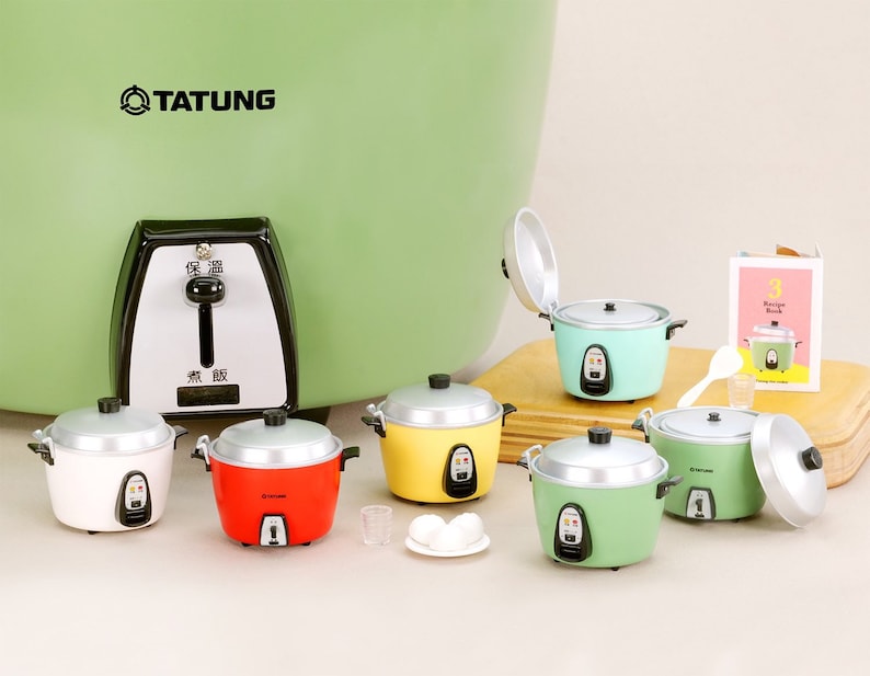 May include: A set of six miniature rice cookers in various colors, including white, red, yellow, and green. The cookers are arranged on a white surface with a small plate of eggs and a glass of water. The cookers have a silver lid and a black base with a button. The image also includes a larger green rice cooker with the word "TATUNG" printed on the front.
