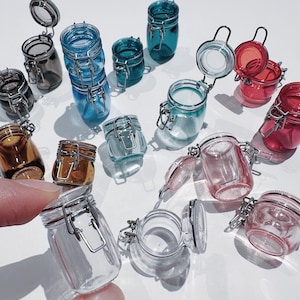 May include: Assortment of small glass jars with metal lids and clasps. The jars are in various colours, including clear, brown, pink, red, and blue.