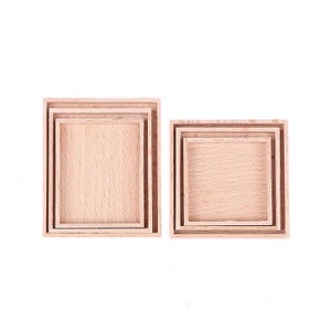 Puede incluir: Conjunto de cuatro bandejas cuadradas de madera encajables. Las bandejas están hechas de madera natural y tienen un color marrón claro. Las bandejas están apiladas una encima de la otra, con la bandeja más grande en la parte inferior y la bandeja más pequeña en la parte superior.