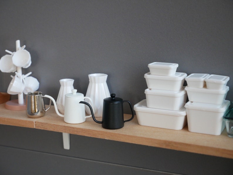 May include: A white shelf with a variety of white kitchenware, including a teapot, a pitcher, and a vase. There are also several white plastic containers stacked on the shelf.