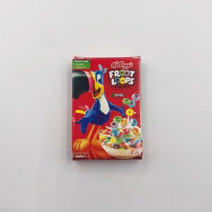 May include: A red Kellogg's Froot Loops cereal box featuring Toucan Sam, a blue toucan with a yellow beak. The box displays a bowl of colorful cereal and the words "Froot Loops". The box is rectangular and sits on a white surface.