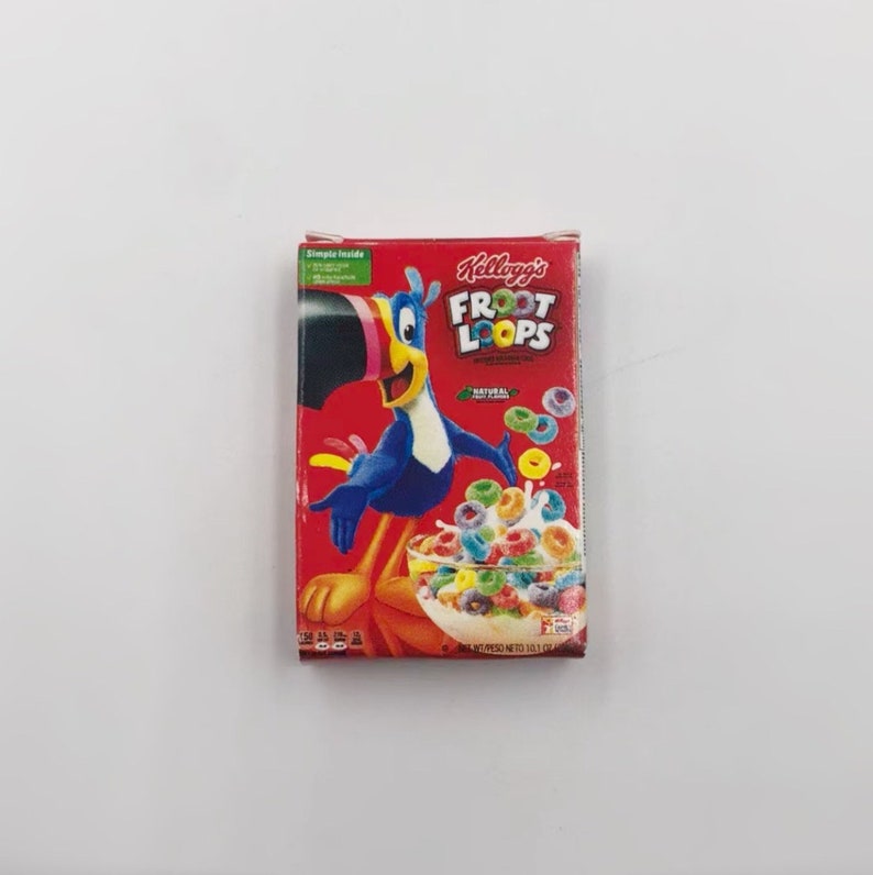 May include: A red Kellogg's Froot Loops cereal box featuring Toucan Sam, a blue toucan with a yellow beak. The box displays a bowl of colorful cereal and the words "Froot Loops". The box is rectangular and sits on a white surface.