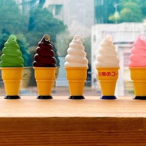 May include: Five miniature ice cream cones in different flavors: green tea, chocolate, vanilla, white chocolate, and strawberry. The cones are all yellow and have a brown base.