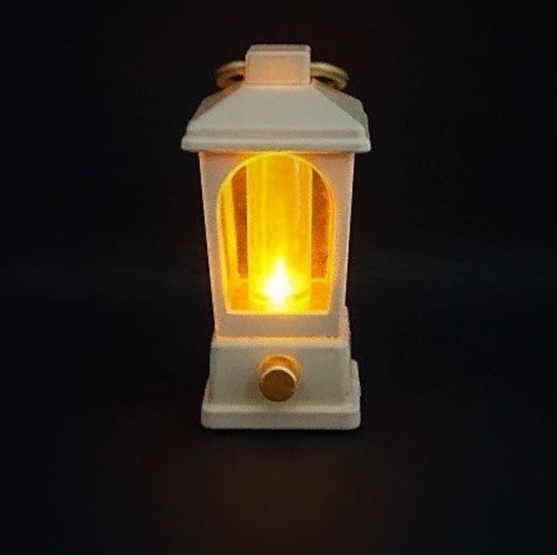 May include: A white lantern with a warm yellow light shining through the glass panels. The lantern has a decorative handle and a small knob on the bottom.