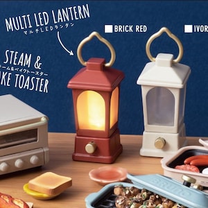 May include: Two miniature LED lanterns, one in brick red and one in ivory, with a gold handle. The lanterns are illuminated and sitting on a wooden surface with other miniature kitchen appliances.