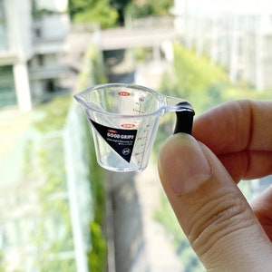 May include: A clear plastic measuring cup with a black handle. The cup has markings for ounces and milliliters. The cup is labeled "GOOD GRIPS" and "OXO".