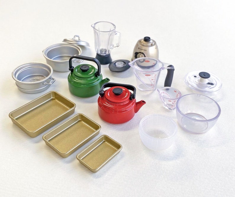 May include: A collection of miniature kitchen appliances and cookware, including a red and green tea kettle, a blender, a food processor, a measuring cup, a baking pan, and a variety of bowls.