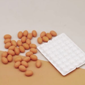 May include: A white egg carton with 30 individual compartments sits on a brown surface. Scattered around the carton are 20 small, brown, oval-shaped eggs.