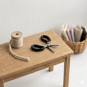 May include: A miniature wooden table holds a spool of twine, a pair of black-handled scissors, and a woven basket filled with fabric swatches. The scissors are open, and the twine extends from the spool. The table is made of light-colored wood.