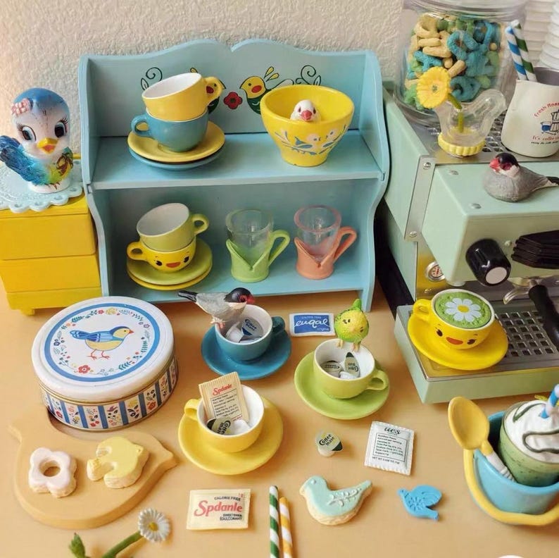 Pode incluir: Um conjunto de ch&aacute; em miniatura caprichoso com decora&ccedil;&otilde;es com tema de p&aacute;ssaros. Inclui x&iacute;caras de ch&aacute;, pires, uma pequena prateleira e uma figura decorativa de p&aacute;ssaro. A paleta de cores apresenta amarelo, azul e verde.