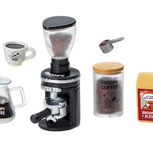 May include: A set of miniature coffee-themed items featuring the Peanuts character Snoopy. The set includes a black coffee grinder, a glass jar of coffee beans, a bag of coffee, a small white coffee cup, and a silver measuring spoon.